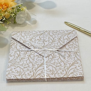 May include: A stack of white envelopes with a gold swirl pattern. The envelopes are tied together with a white ribbon.