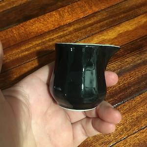 May include: A small black ceramic creamer with a white rim. The creamer is shaped like a pitcher with a small spout.