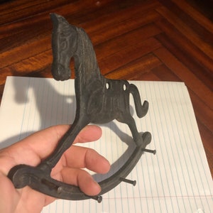 May include: Black cast iron rocking horse key holder with five hooks. The horse is in a rocking position with a curved base.