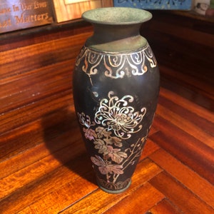 May include: A black vase with a crack down the side, decorated with iridescent mother-of-pearl floral designs.