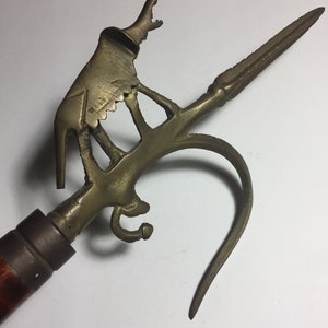 May include: A brass walking stick with a decorative animal head handle and a long, pointed tip. The handle is shaped like a stylized animal with a long, curved neck and a small, round head. The tip of the stick is sharp and pointed.