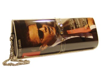 May include: A rectangular clutch bag featuring a photographic print of a person wearing sunglasses. The bag has a clear plastic overlay with small decorative rhinestones and a silver-toned metal chain strap attached to the side.