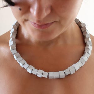 Può includere: Una collana di cemento bianco con perline a forma quadrata. La collana è indossata da una persona con una carnagione chiara.