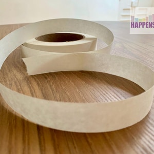 May include: A roll of white paper tape on a wooden surface. The tape is unrolled and the end is curled up.