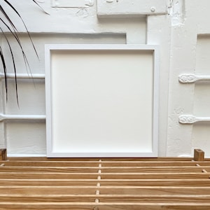 May include: A white picture frame with a white mount, sitting on a wooden slatted surface.