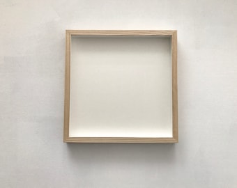 以下が含まれることがあります： 白いマットが付いたシンプルな明るい木製の額縁。フレームは正方形で、クリーンでモダンなデザインです。