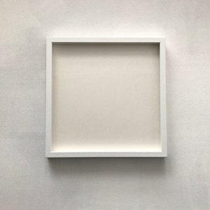 Puede incluir: Un marco de fotos blanco con un paspartú blanco, colgado en una pared blanca.