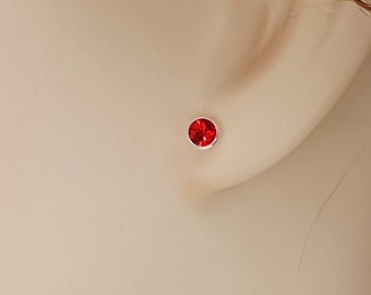 Może przedstawiać: Zbliżenie na kolczyk z czerwonym kamieniem szlachetnym. Kolczyk jest osadzony w srebrnej oprawie.