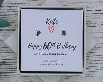 Może przedstawiać: Białe pudełko prezentowe z kartą w środku, na której napisano "Kate Happy 60th Birthday Love Donna, Paul & family xx Sterling Silver www.newforestgift.co.uk" oraz dwa małe srebrne kolczyki w kształcie serca.
