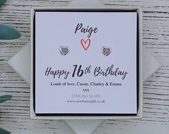 Może przedstawiać: Białe pudełko prezentowe z kartą w środku, na której napisano "Paige Happy 16th Birthday Loads of love, Cassie, Charley & Emma XXX STERLING SILVER www.newforestgift.co.uk" oraz dwa srebrne kolczyki w kształcie serca.