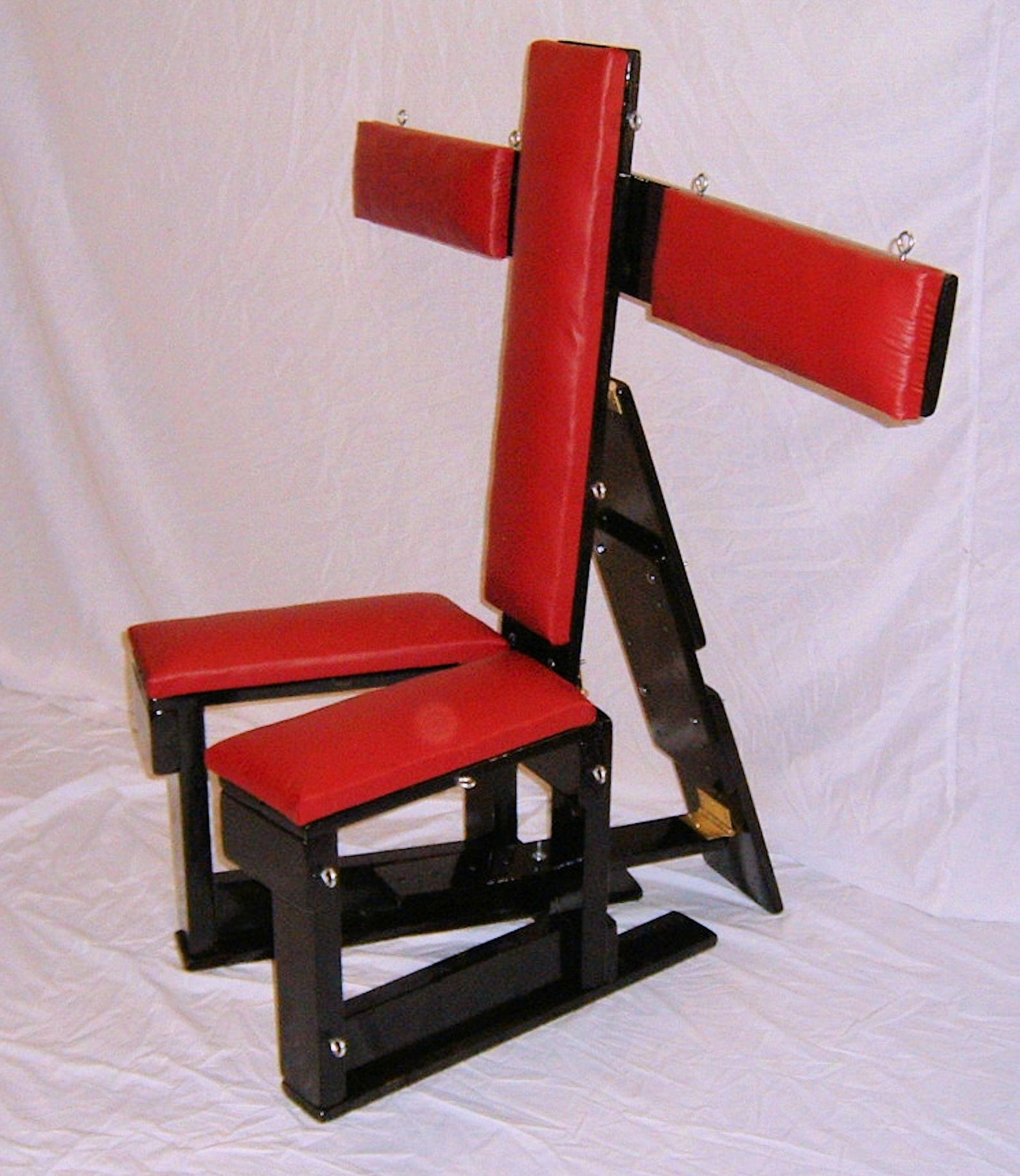 Fully adjustable red and black bdsm bondage chair with padded restraints and multiple tie-down points for dungeon use.
