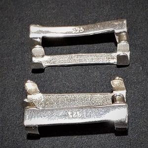 May include: Two silver metal clasps with the markings "925" on each. The clasps are designed to be used for jewelry or other items.