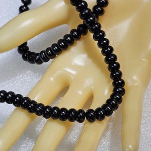 May include: A black beaded bracelet and necklace set. The beads are small, round, and have a glossy finish. The jewelry is displayed on a mannequin hand.