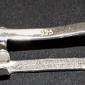 May include: A silver-toned metal clasp with a rectangular shape and a '925' marking. The clasp is designed to connect two pieces of jewelry.