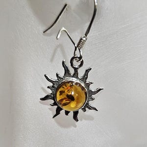May include: Silver sun earrings with a round amber stone in the center.