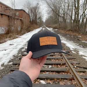 May include: Black baseball cap with a brown leather patch that says "Salty Cows est. 2018" and a small cow silhouette.