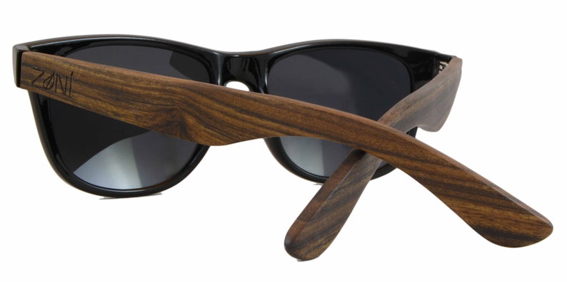 May include: Black sunglasses with dark lenses and wooden arms. The arms are made of dark brown wood with a natural grain pattern. The brand name "Zani" is engraved on the left arm.