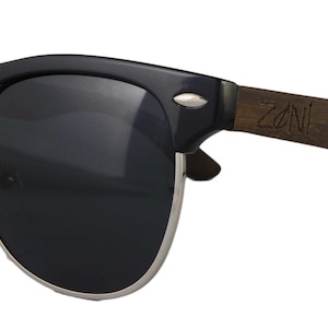 Puede incluir: Gafas de sol negras con montura de madera. La montura est&aacute; grabada con la palabra "ZONI".