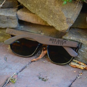 Puede incluir: Gafas de sol de madera con lentes negros y el texto "MRS BUCK 11-17-17" grabado en la montura.