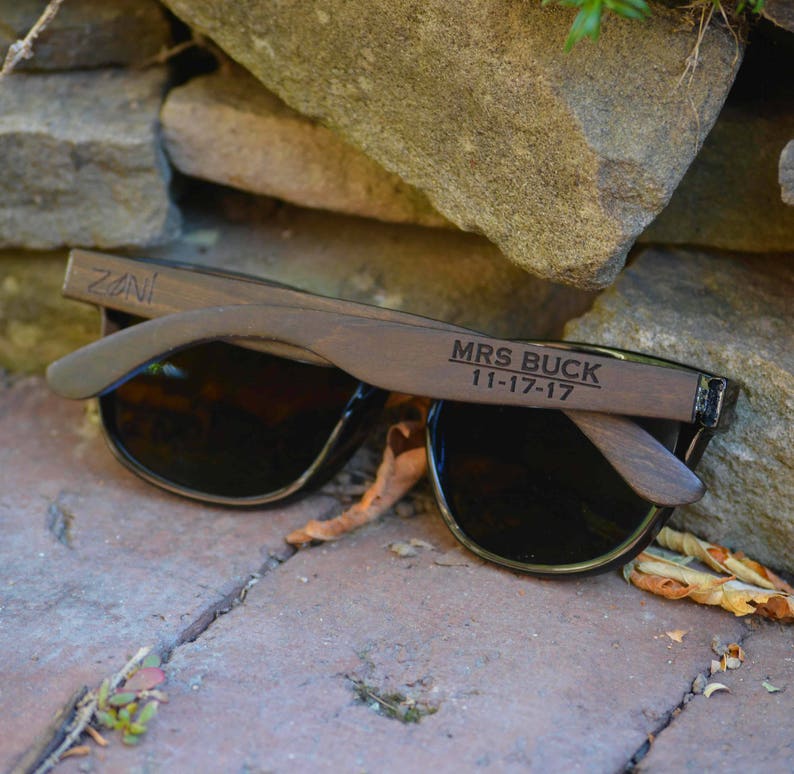 Puede incluir: Gafas de sol de madera con lentes negros y el texto "MRS BUCK 11-17-17" grabado en la montura.