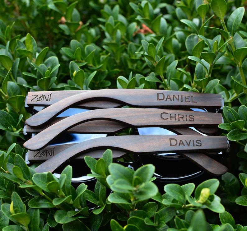 May include: Four pairs of dark brown wooden sunglasses with the names "Zoni", "Daniel", "Chris", and "Davis" engraved on them.