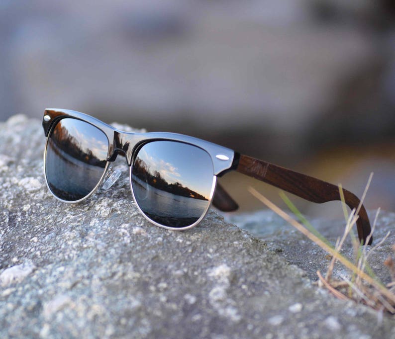 Puede incluir: Gafas de sol negras con lentes espejados y un marco de madera. Las gafas de sol est&aacute;n apoyadas en una roca gris.