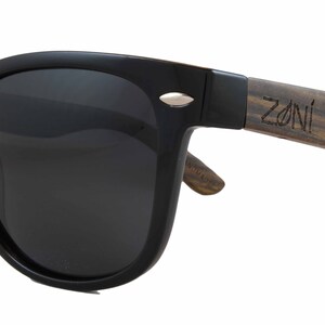 May include: Black sunglasses with a wooden frame. The frame is brown with a wood grain pattern and has the word "ZONI" engraved on it.