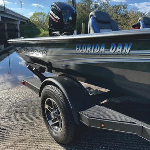 Puede incluir: Un barco negro y plateado con un motor fuera de borda Mercury. El barco est&aacute; en un remolque con una rueda negra y una defensa negra. El barco tiene las palabras "Florida Dan" escritas en el lateral.