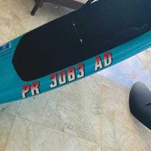 Puede incluir: Una tabla de surf el&eacute;ctrica azul y negra con una pegatina roja y blanca que dice "PR 3083 AD".