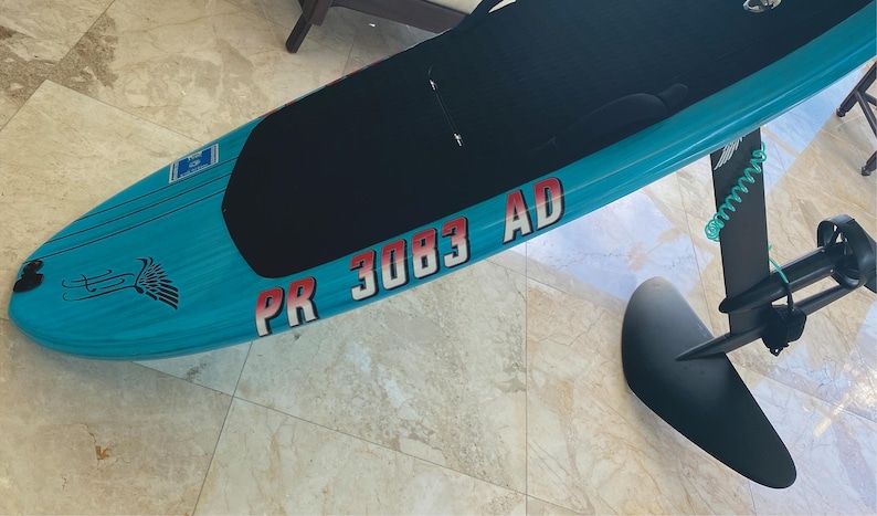 Puede incluir: Una tabla de surf el&eacute;ctrica azul y negra con una pegatina roja y blanca que dice "PR 3083 AD".
