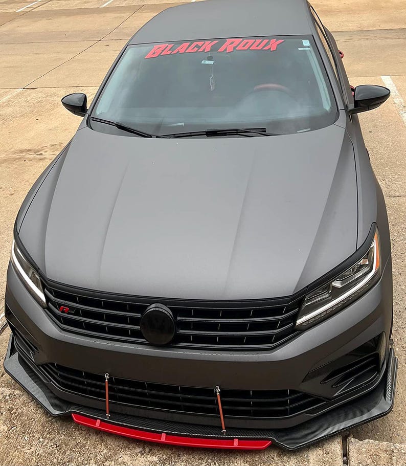 May include: A gray Volkswagen Passat with a black grille and a red "BLACK ROUX" windshield banner. The car has a black front splitter with a red lip.