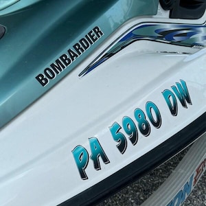 Puede incluir: Una moto acu&aacute;tica blanca y turquesa con la palabra "BOMBARDIER" en letras negras en el lateral y la matr&iacute;cula "PA 5980 DW" en letras turquesa en la parte trasera.