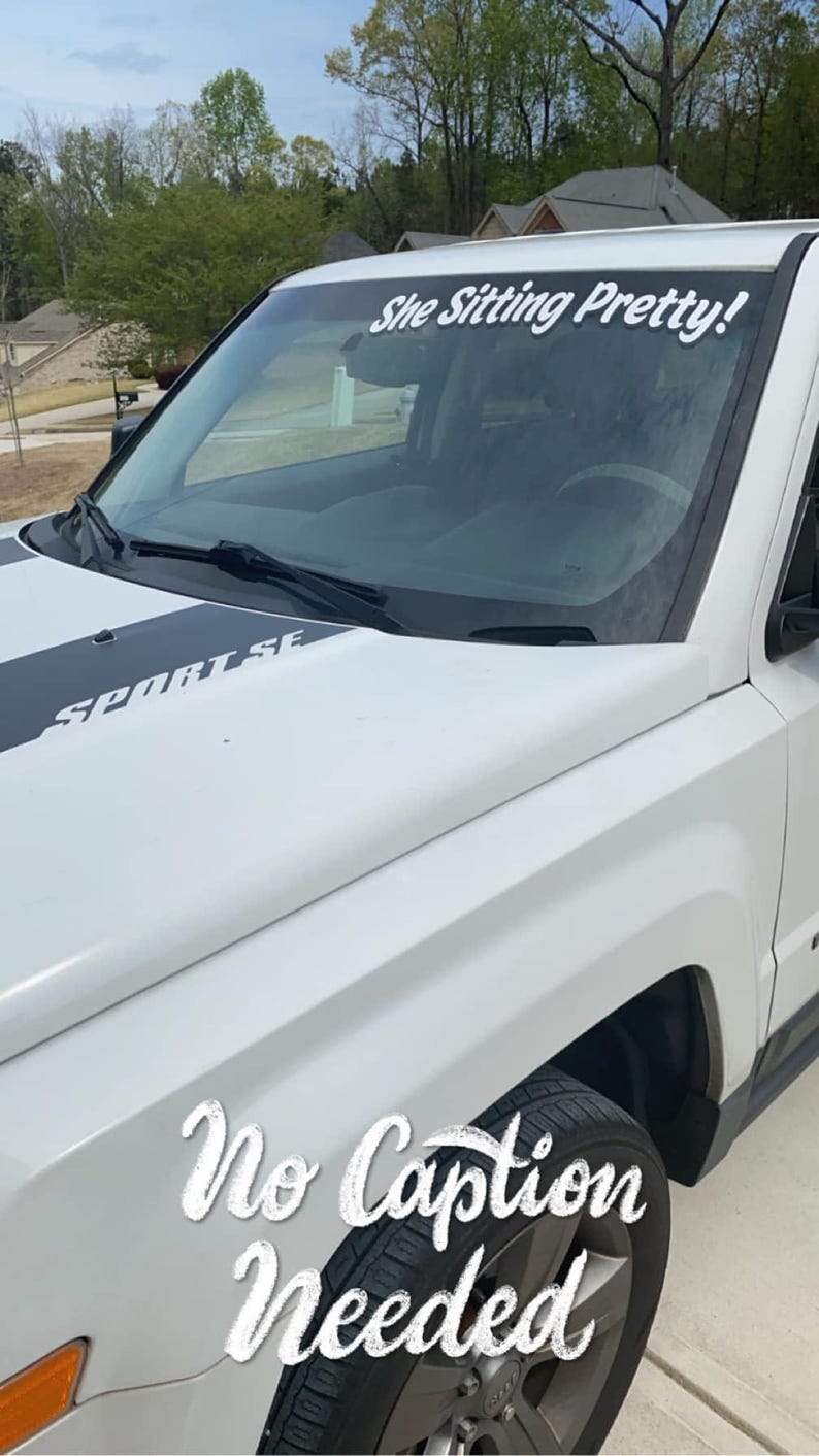 May include: White Jeep with a black and gray stripe on the hood. The windshield has a white decal that says "She Sitting Pretty!" The car has a black bumper and black wheels. The text "No Caption Needed" is written on the side of the car.