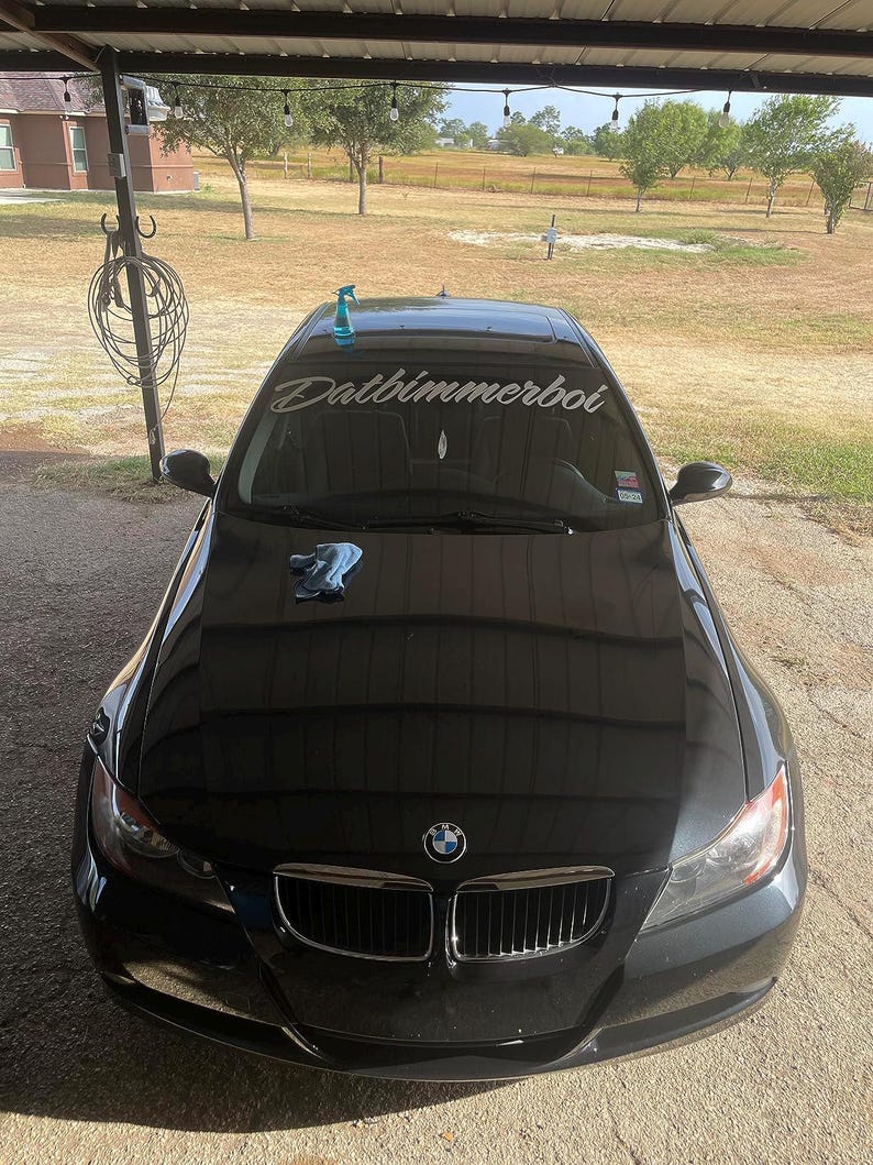 May include: A black BMW 3 series car with a custom windshield banner that reads "Datbimmerboi".