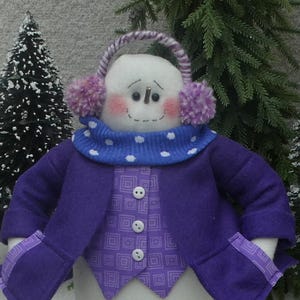 May include: A purple snowman wearing a blue and white polka dot scarf, a purple vest with a geometric pattern, and purple earmuffs with pink pom-poms.