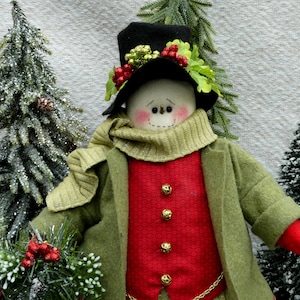 Könnte beinhalten: Eine handgefertigte Schneemannfigur, bekleidet mit einem grünen Mantel, einer roten Weste und einem schwarzen Zylinder, verziert mit Beeren und Grünzeug. Der Schneemann hat ein gesticktes Lächeln und rosige Wangen, ideal für Weihnachtsdekorationen.