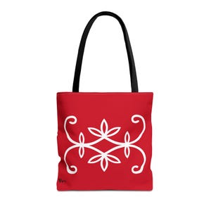 May include: A red tote bag featuring a white symmetrical floral-inspired graphic design centered on the front. The bag has two black shoulder straps attached to the top. A small black signature mark is visible in the bottom left corner.