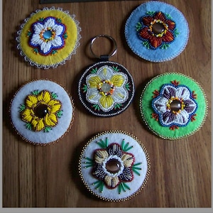 May include: Six beaded flower keychains with different colored backgrounds and bead patterns. The keychains are round and feature a variety of colors, including white, yellow, green, blue, red, and brown.
