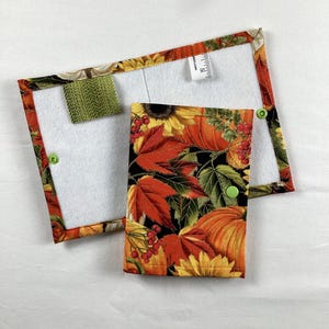 May include: A rectangular fabric pouch with a fall-themed print featuring pumpkins, sunflowers, and red berries on a black background. The interior is white felt with a green fabric tab and a small white tag showing 5 inches of measurement.