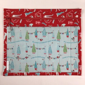 May include: A rectangular Christmas-themed quilted pouch with a red zipper and a snowflake charm. The pouch features a light blue background with Christmas trees, lights, and text that reads "wonderful time of the year". The border is red with holiday-themed patterns.