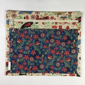 Puede incluir: Una bolsa rectangular de tela con cierre de cremallera. La secci&oacute;n superior presenta un fondo crema con patrones de p&aacute;jaros y flores rojos y azules. La secci&oacute;n principal tiene un fondo azul con flores rojas y hojas verdes.