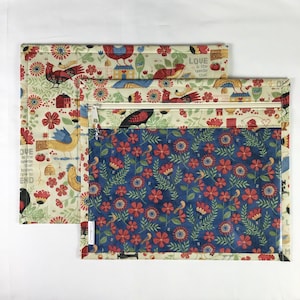 Puede incluir: Dos bolsas de tela con cierres de cremallera. Una bolsa presenta un fondo crema con p&aacute;jaros, flores y casas rojas, azules y amarillas. La otra bolsa tiene un estampado floral azul con flores rojas. El texto "LOVE is the needle that knows how to END" es visible.
