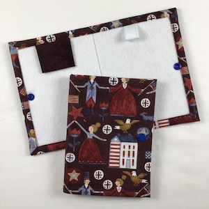 May include: A rectangular, white felt board with a brown fabric border and a small, matching brown square attached. A smaller, rectangular fabric case with a patriotic print featuring figures, flags, and stars is also present.