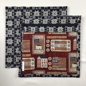 May include: Two square quilted pouches. One features a red, white, and blue patriotic design with text that reads "Broad Stripes", "Bright Stars", "Old Glory", and "In God is our trust". The other has a black and gray geometric pattern.