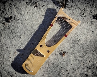 May include: A wooden lyre with strings and red accents. The lyre is lying on a gray, textured surface.
