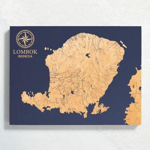 Könnte beinhalten: Eine Holzkarte von Lombok, Indonesien, mit marineblauem Hintergrund. Die Topographie der Insel ist in hellbrauner Holzmaserung detailliert dargestellt. Der Text "LOMBOK INDONESIA" befindet sich über einer Windrose.