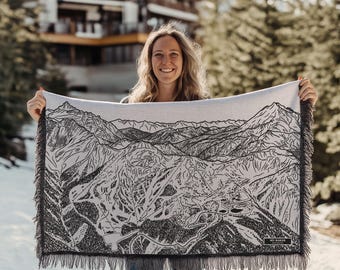 May include: A woman holds a white and black woven throw blanket with a detailed map of a mountain range. The map is in black and white and includes the text "Mt. Baker".