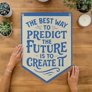 May include: A banner with the text "THE BEST WAY TO PREDICT THE FUTURE IS TO CREATE IT" in blue lettering. The banner has a cream-colored background with a blue border and grommets. The banner is displayed on a wooden surface.