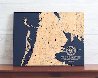 Puede incluir: Un mapa de madera de Clearwater, Florida, con una rosa de los vientos y el texto "CLEARWATER, GULF COAST - UNITED STATES, FLORIDA". El mapa está sobre un fondo azul.