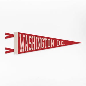 May include: A red pennant with the text "WASHINGTON D.C." in white block letters. The pennant is triangular, with two red ribbons attached to the left side. The background is white.